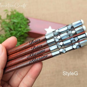 May include: Four wooden chopsticks featuring a dark brown finish and a decorative handle inlaid with iridescent mother-of-pearl mosaic pieces. Each chopstick is engraved with the name Peter or Akarami in a black script font.
