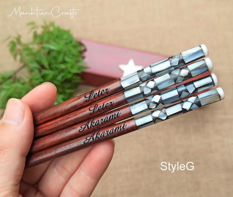 May include: Four wooden chopsticks featuring a dark brown finish and a decorative handle inlaid with iridescent mother-of-pearl mosaic pieces. Each chopstick is engraved with the name Peter or Akarami in a black script font.