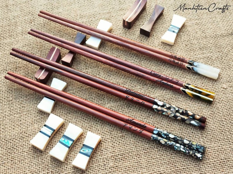 Puede incluir: Cuatro pares de palillos de madera personalizados con puntas decorativas. Cada par tiene un nombre diferente y caracteres japoneses grabados. Los palillos est&aacute;n apoyados en reposapalillos de cer&aacute;mica blanca.