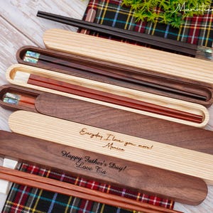 May include: A collection of wooden chopstick sets with matching cases. Some cases are light wood, others are dark wood. Two cases feature engraved text: "Everyday I love you more! Monica" and "Happy Father's Day! Love Tia." The chopsticks have inlaid details.