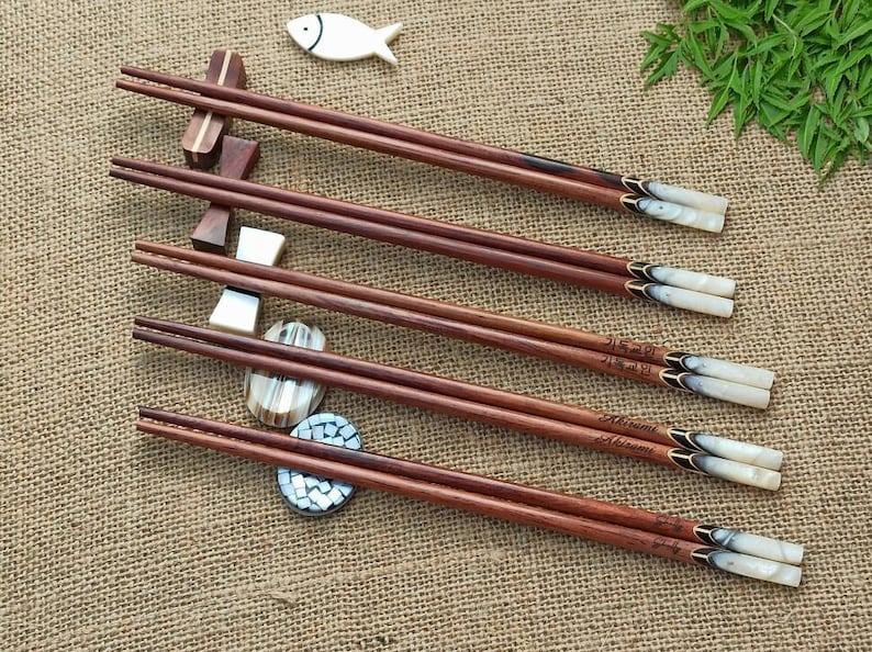 Puede incluir: Conjunto de seis pares de palillos de madera con puntas decorativas de n&aacute;car. Cada par tiene una inscripci&oacute;n diferente en los palillos.