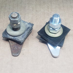 May include: Two metal brackets with bolts, nuts, washers, and rubber pads. One bracket has a rusty, angled metal piece, while the other has a shiny, angled metal piece. The hardware is silver and gold.