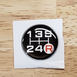 May include: A black and silver 5-speed manual transmission gear shift pattern sticker with a red "R" for reverse.