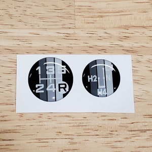 May include: Two black and white round stickers with gear shift patterns. One sticker shows the numbers 1, 2, 3, 4, 5, and R. The other sticker shows H2, N, and H4.