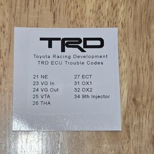 May include: A white card with the TRD logo and text, "Toyota Racing Development TRD ECU Trouble Codes." The card lists various trouble codes, including 21 NE, 23 VG In, 24 VG Out, 25 VTA, 26 THA, 27 ECT, 31 OX1, 32 OX2, and 34 9th Injector.