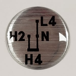 May include: A silver round sticker with a black gear shift pattern. The pattern shows the letters H2, N, L4, and H4.
