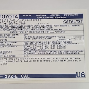 May include: A white Toyota emissions control label with blue text and a black border. The label includes information about the engine family, EVAP family, EFI, and other specifications. The label also includes the text "CATALYST" and "3VZ-E CAL".