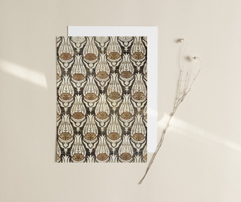 May include: A white card with a black and white print of a repeating pattern of stylized tulips. The tulips are outlined in black and have a brown and white center. The card is on a beige background.
