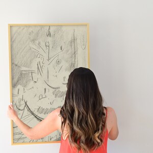 Peut inclure: Un croquis au fusain encadr&eacute; d'un sapin de No&euml;l. L'&oelig;uvre est dans un cadre dor&eacute; et tenue par une personne. L'esquisse est dans des tons de gris et de noir, avec un style minimaliste. Le fond est un mur blanc uni.