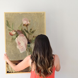 May include: A framed painting of a still life featuring pink peonies in a glass vase. The painting is on a light green background with a brown table.
