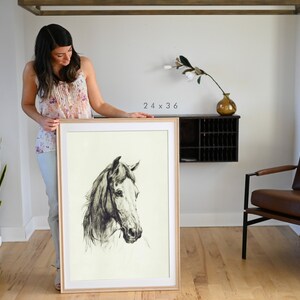 May include: A framed black and white drawing of a horse's head. The drawing is on a cream-colored background and is framed in a natural wood frame. The frame is 24 x 36 inches.