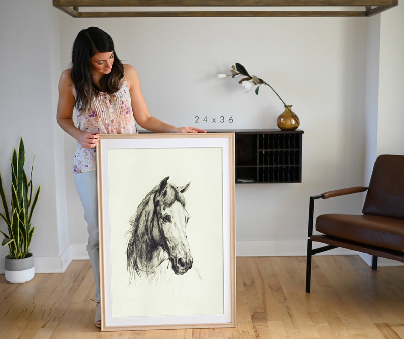 May include: A framed black and white drawing of a horse's head. The drawing is on a cream-colored background and is framed in a natural wood frame. The frame is 24 x 36 inches.
