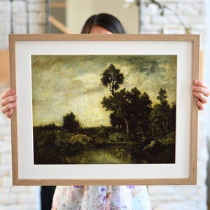 May include: A framed painting of a landscape with a river, trees, and a cloudy sky. The painting is in a light wood frame.
