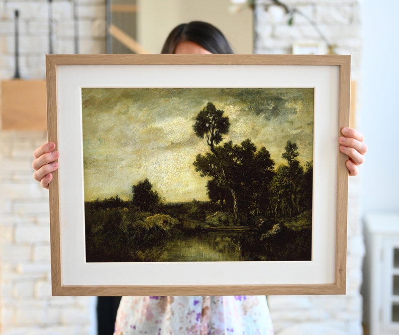 May include: A framed painting of a landscape with a river, trees, and a cloudy sky. The painting is in a light wood frame.