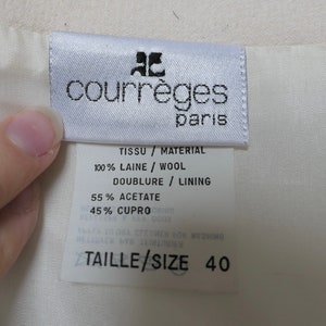 May include: A close-up of a white fabric tag with the brand name "courr&egrave;ges paris" in black text. The tag also includes fabric composition details: 100% wool, 55% acetate, and size 40.