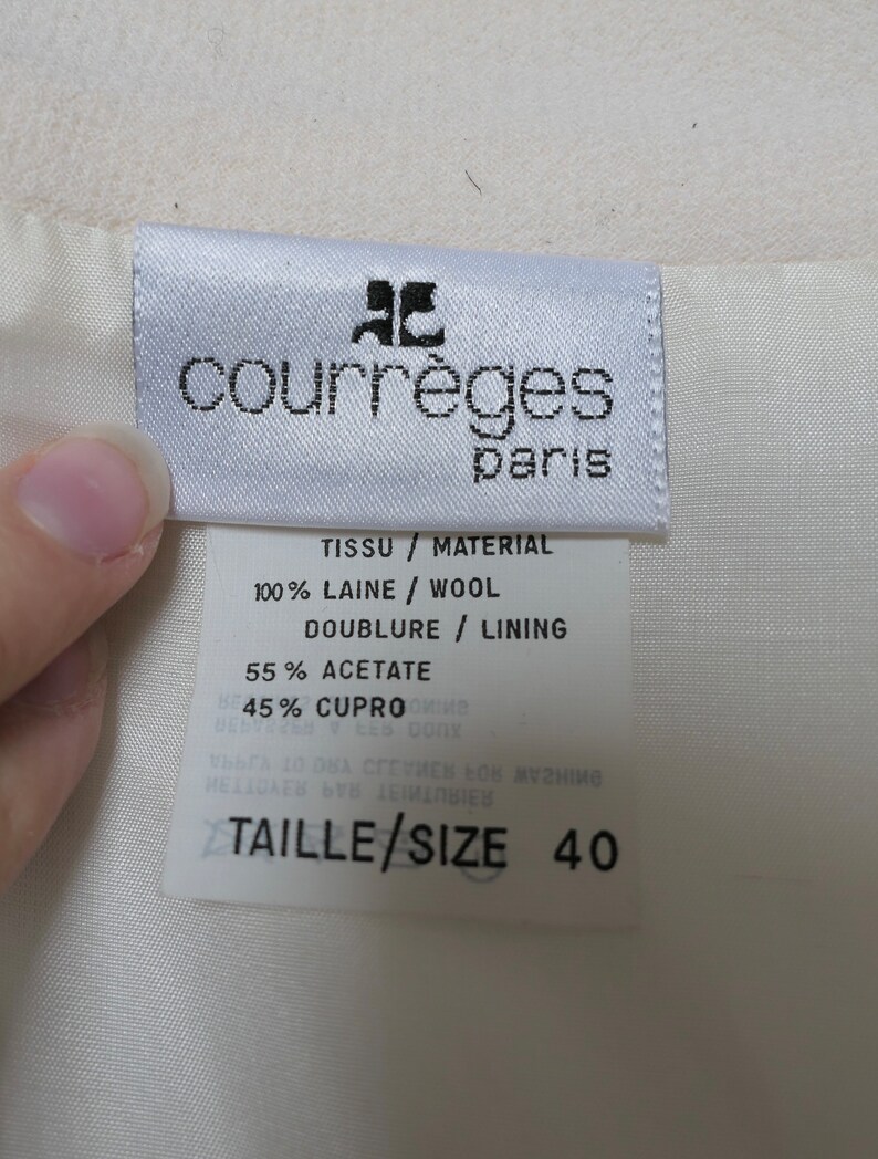 May include: A close-up of a white fabric tag with the brand name "courr&egrave;ges paris" in black text. The tag also includes fabric composition details: 100% wool, 55% acetate, and size 40.