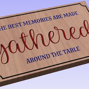 May include: Wooden sign with a black frame and the text "The best memories are made gathered around the table". The word "gathered" is in red and the rest of the text is in blue.