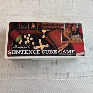 May include: A vintage Scrabble Sentence Cube Game box. The box has a retro design with the game's name. The image on the box shows game pieces, books, and a couple playing. The box is white with a black and red design. The game was made in 1971.
