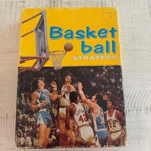 May include: Vintage basketball strategy game box with a yellow background and blue text. The box features a basketball net and players in action. The game's title, "Basketball Strategy," is prominently displayed. The image shows a basketball game in progress.