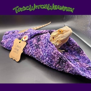 May include: A purple and black lizard wrap made of crushed velvet. The wrap is designed to provide a cozy and safe space for a lizard to rest. The wrap is labeled "Lizard Wrap" and "Crushed Violet".