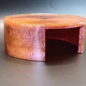 May include: A round, hollow, copper-colored, decorative object with a smooth, shiny surface. The object has a cut-out section on one side, creating a semi-circular opening.