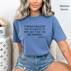 May include: A blue washed denim t-shirt with a quote from Shakespeare: "I would challenge you to a battle of wits, but I see you are unarmed."