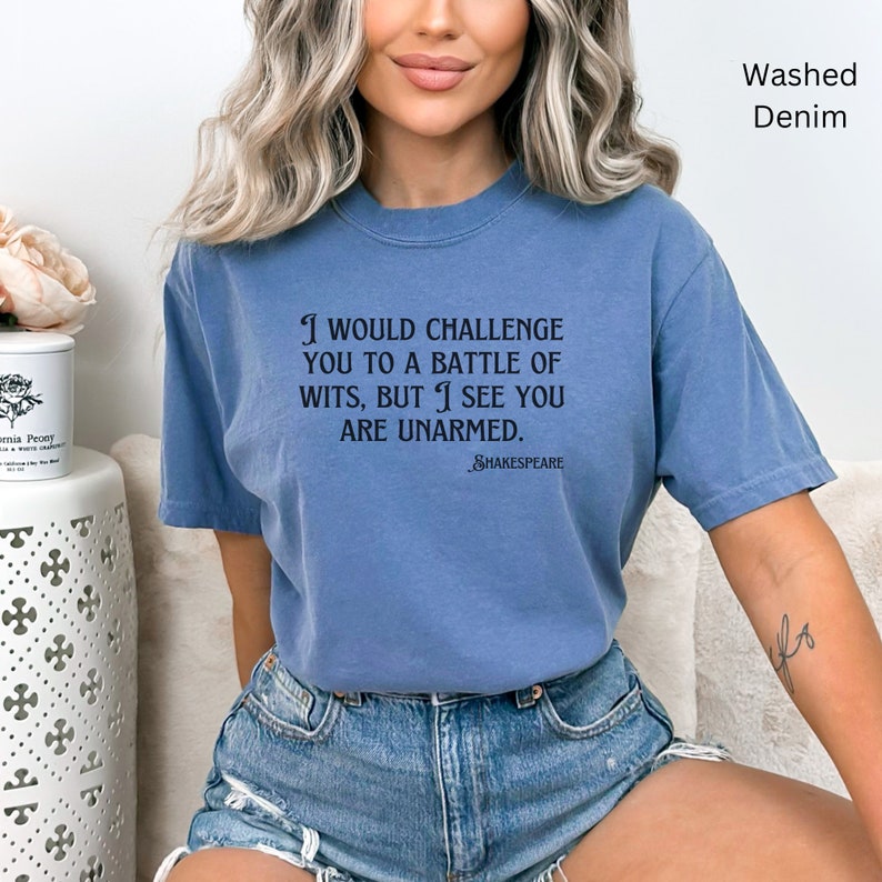 May include: A blue washed denim t-shirt with a quote from Shakespeare: "I would challenge you to a battle of wits, but I see you are unarmed."