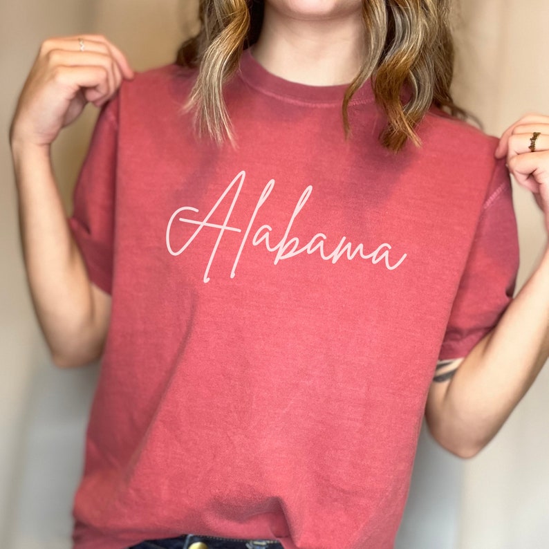 May include: A red t-shirt with the word "Alabama" written in white cursive script.
