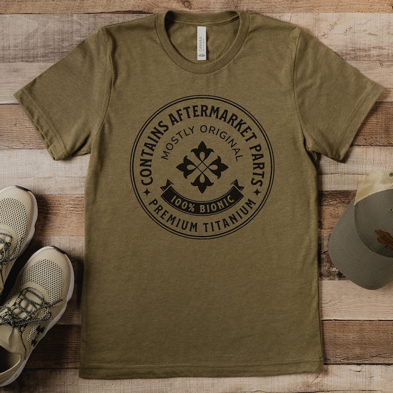 Puede incluir: Una camiseta verde con un gr&aacute;fico circular negro que dice "Contiene piezas de recambio" con un dise&ntilde;o de flor estilizado y el texto "Mayormente original, 100% Bi&oacute;nico, Titanio de primera calidad".