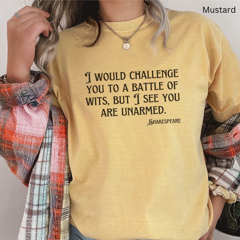 May include: A mustard yellow t-shirt with a black graphic print that reads "I would challenge you to a battle of wits, but I see you are unarmed. -Shakespeare".