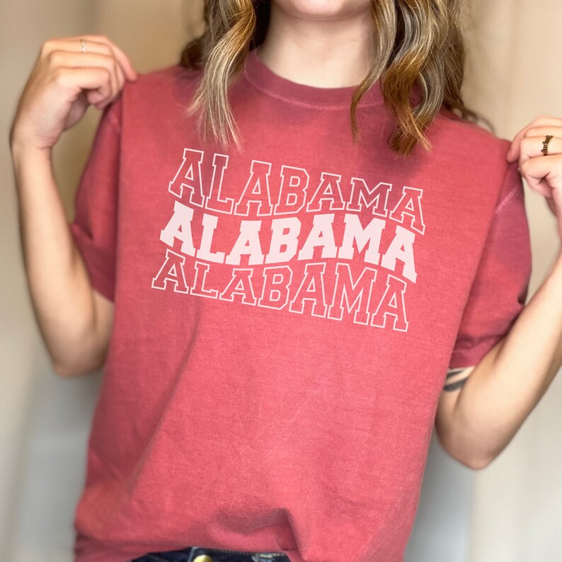May include: A red t-shirt with the word "ALABAMA" printed three times in white, with each word slightly offset from the one above it.