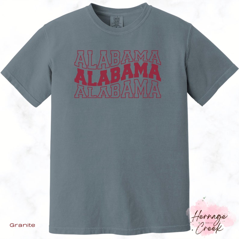 May include: A granite grey t-shirt with the word "ALABAMA" repeated three times in a stacked, red, outlined font.