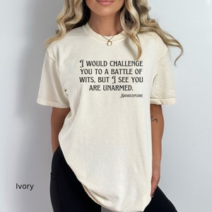 May include: Ivory t-shirt with a black print that reads "I would challenge you to a battle of wits, but I see you are unarmed." The text is attributed to Shakespeare.