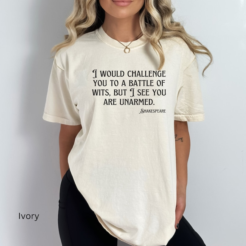 May include: Ivory t-shirt with a black print that reads "I would challenge you to a battle of wits, but I see you are unarmed." The text is attributed to Shakespeare.