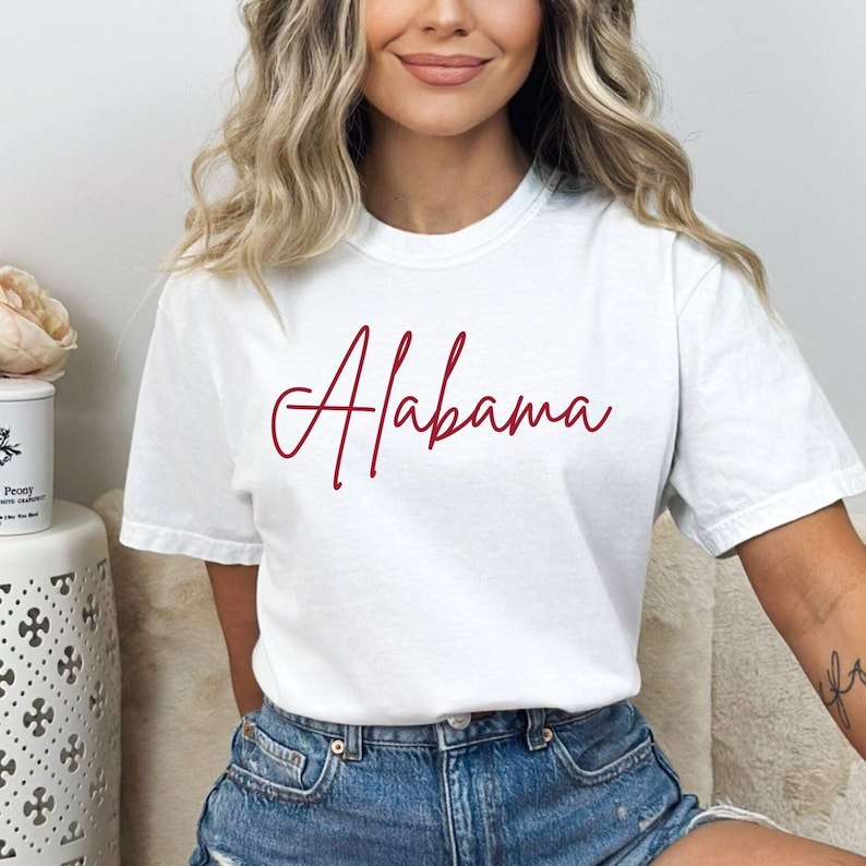 May include: White t-shirt with a red cursive script that says "Alabama".