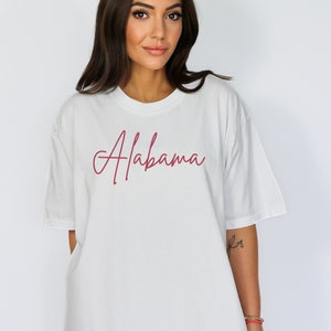 May include: White oversized t-shirt with a red cursive script that says "Alabama".