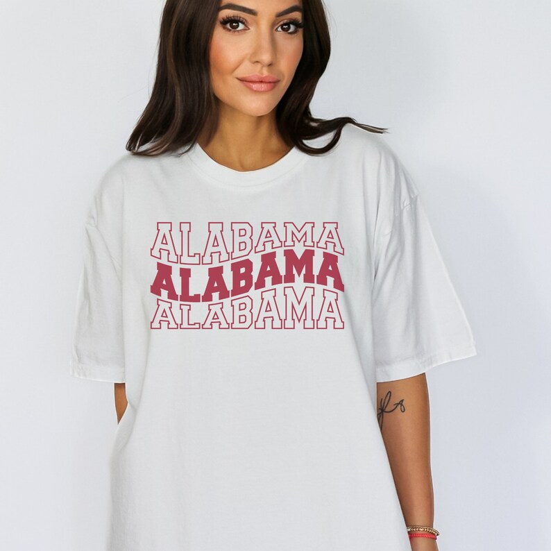 May include: White oversized t-shirt with a red graphic print of the word "Alabama" repeated three times in a stacked design.