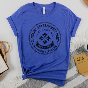 Puede incluir: Una camiseta azul real con un gr&aacute;fico circular negro que dice "Contiene piezas de recambio, principalmente originales, 100% Bi&oacute;nico, Titanio de primera calidad".