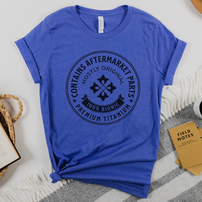 Puede incluir: Una camiseta azul real con un gr&aacute;fico circular negro que dice "Contiene piezas de recambio, principalmente originales, 100% Bi&oacute;nico, Titanio de primera calidad".