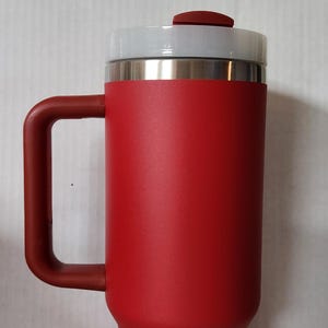 May include: A white ceramic mug with a black handle and the text "But First, Coffee" in a bold, black font. The mug is set against a neutral background, highlighting its simple design.