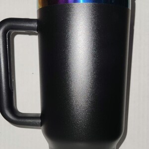 May include: A black travel mug with a black handle and a rainbow iridescent band around the lid.