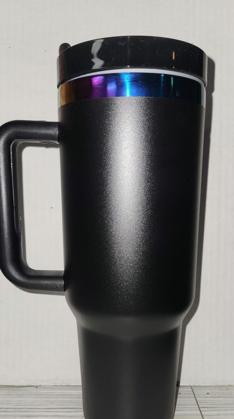 May include: A black travel mug with a black handle and a rainbow iridescent band around the lid.
