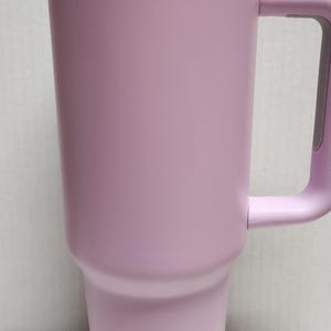May include: A lavender travel mug with a white lid and a rainbow iridescent band around the top. The mug has a handle.