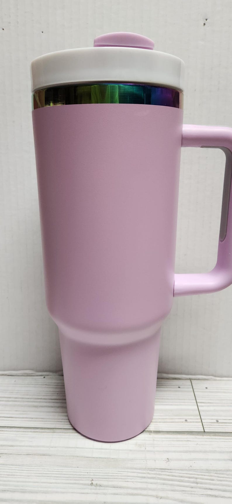 May include: A lavender travel mug with a white lid and a rainbow iridescent band around the top. The mug has a handle.