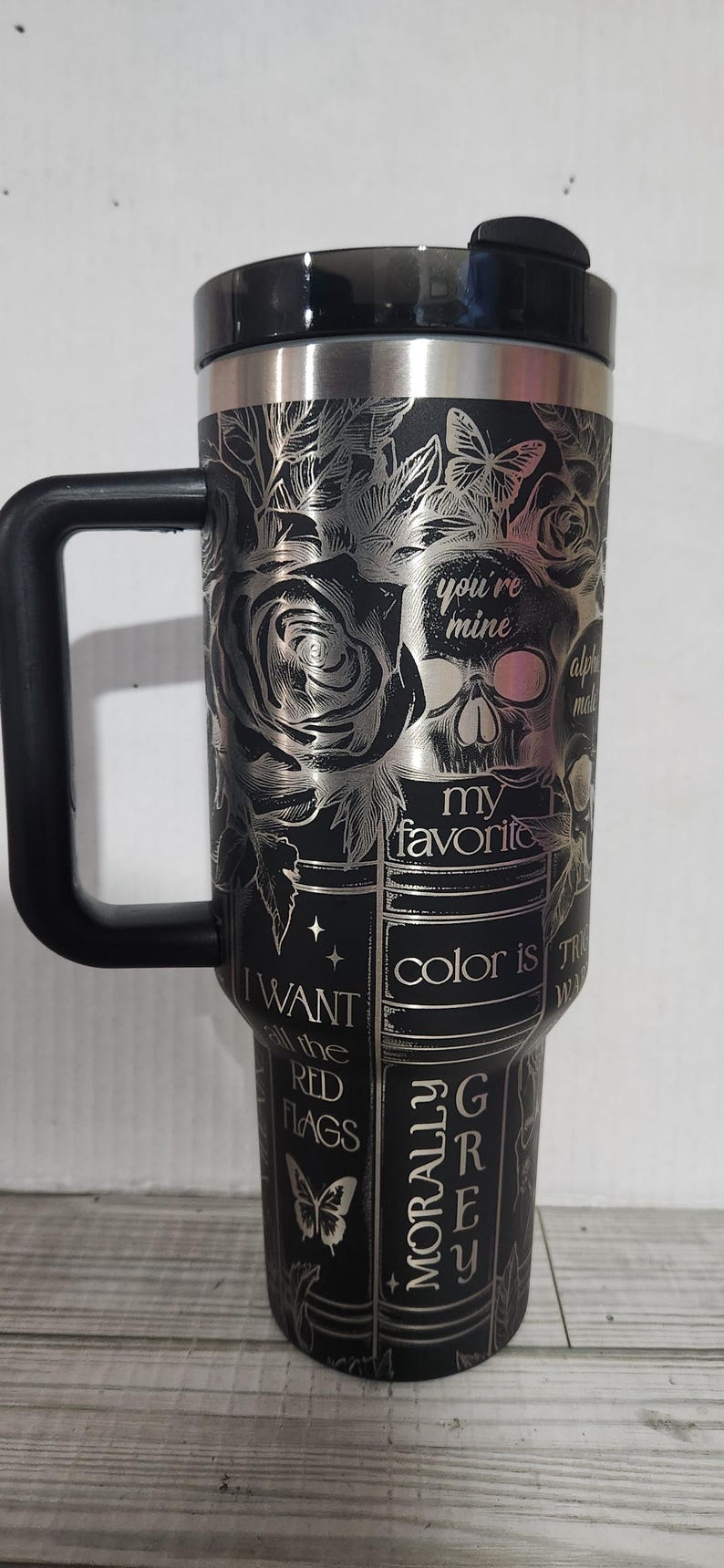 May include: Black travel mug with a silver floral and skull design. The mug has a black handle and lid. Text includes "you're mine", "my favorite color is grey", and "I want all the red flags".