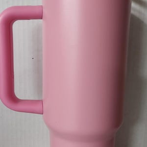 May include: A pink stainless steel travel mug with a gold rim and a pink lid. The mug has a handle and is designed to keep drinks hot or cold.