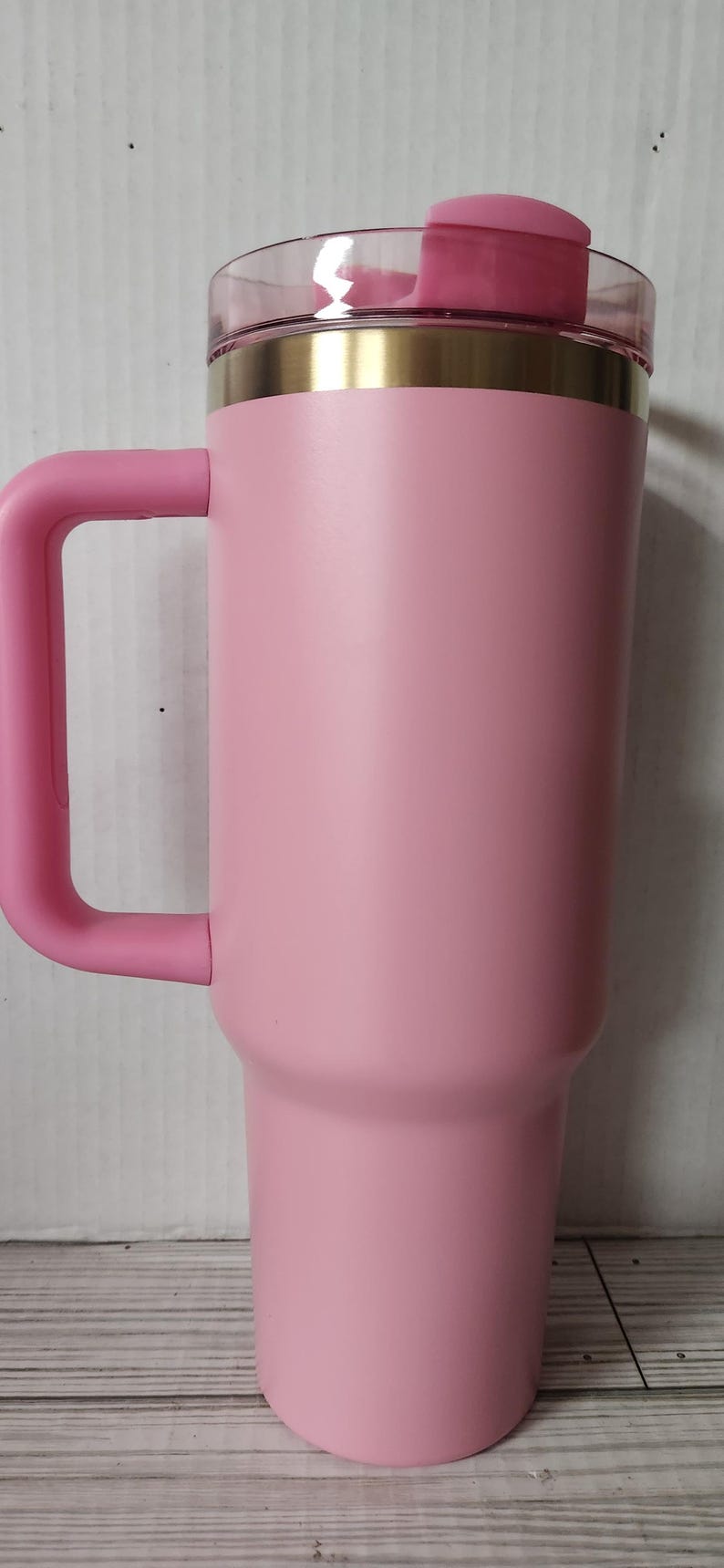 May include: A pink stainless steel travel mug with a gold rim and a pink lid. The mug has a handle and is designed to keep drinks hot or cold.