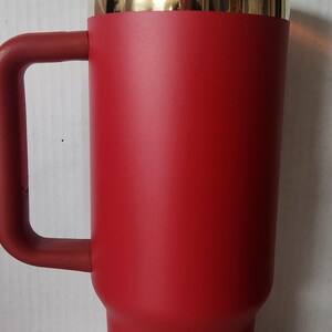 May include: A red travel mug with a gold rim and a brown lid. The mug has a handle and is made of stainless steel.