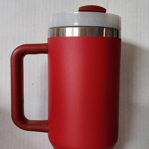 May include: A red travel mug with a lid and a handle. The mug is made of stainless steel and has a matte finish.