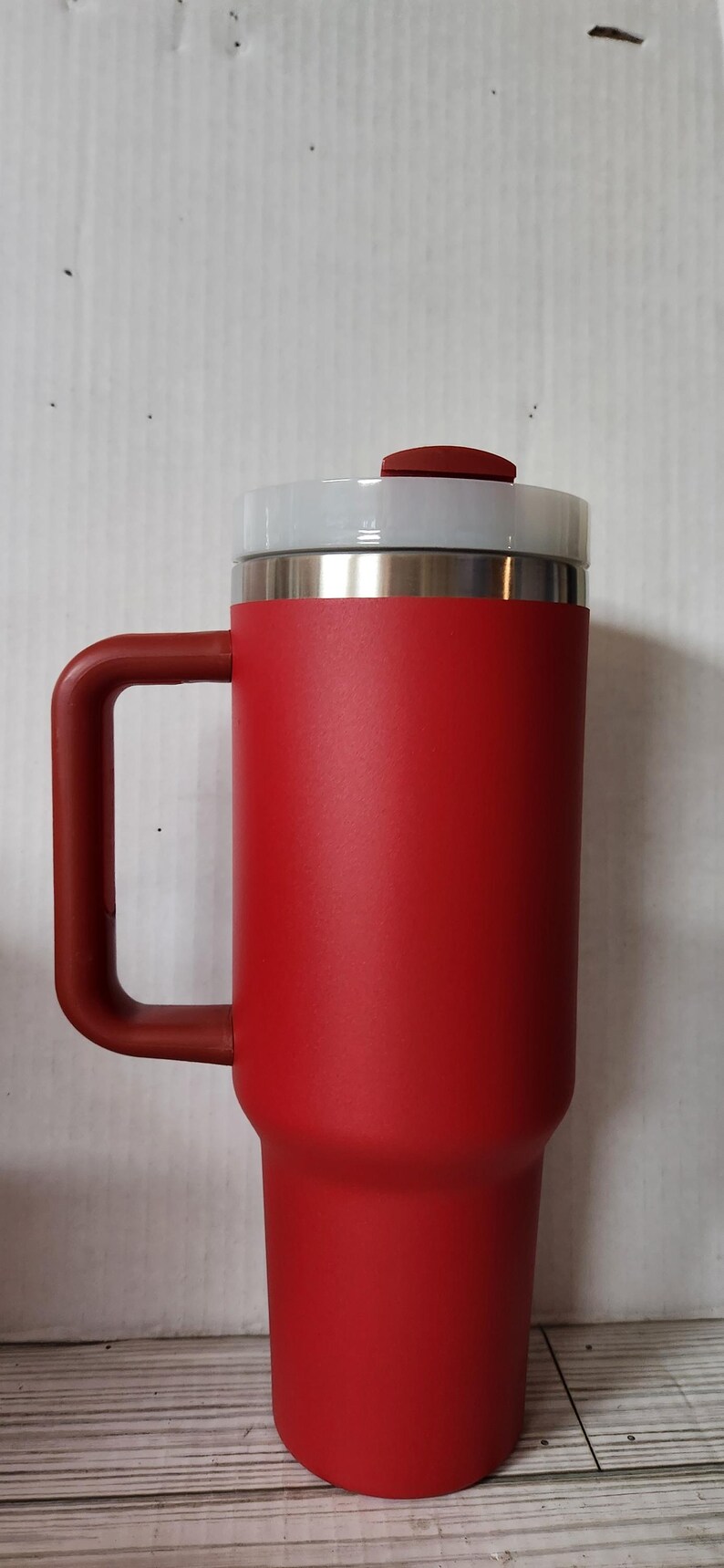 May include: A red travel mug with a lid and a handle. The mug is made of stainless steel and has a matte finish.